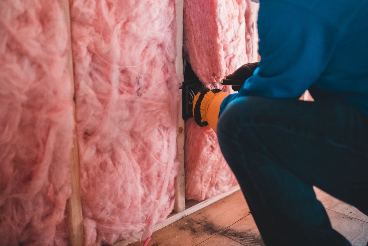 Worker installing blown-in insulation in a residential attic, showing loose-fill material between joists